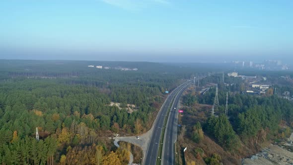 Aerial Drone Footage. Fly Over Autobahn Near Forest with Town on Horizon.