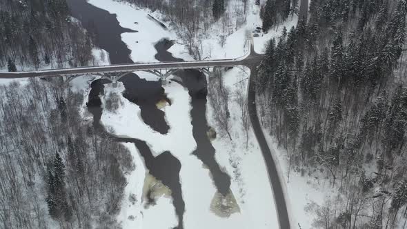 High Aerial View of a bridge over river Gauja in  Sigulda, Latvia in a snowstorm alt