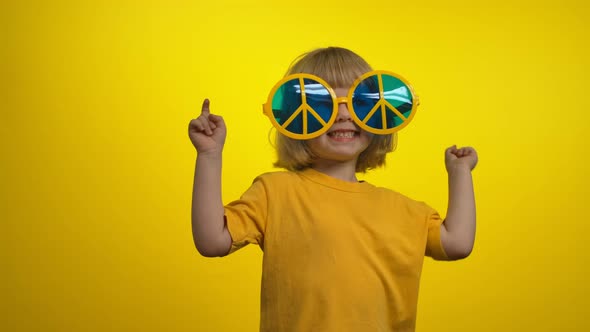 Little Girl in Yellow Sunglasses is Dancing and Smiling on the Yellow Background alt