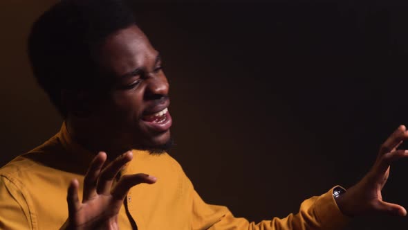 Stylish African American Man in Yellow Shirt Emotionally Sings a Song and Gestures with His Hands alt
