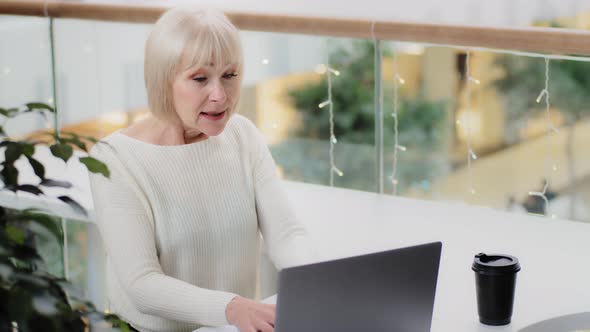 Excited Excited Middle Aged Caucasian Woman Sitting at Desk Using Laptop Intently Playing Computer alt