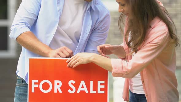 Young Man and Woman Setting for Sale Sign in House Yard, Young Family Relocation alt