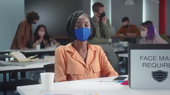 A Young African Professor is Sitting in a Blue Protective Mask with Her Students in the Classroom alt
