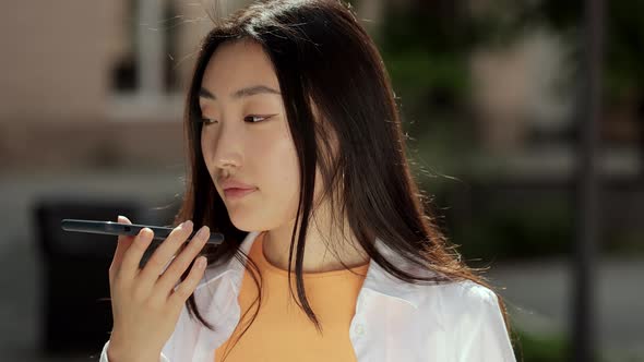 Happy Young Asian Woman Sending Audio Voice Message on Cellphone at Outdoor Talking to Mobile alt