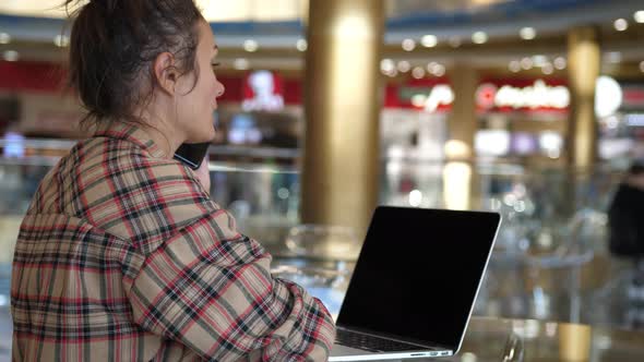 Caucasian Woman Talking By Phone During Working with Laptop in Coffee Shop