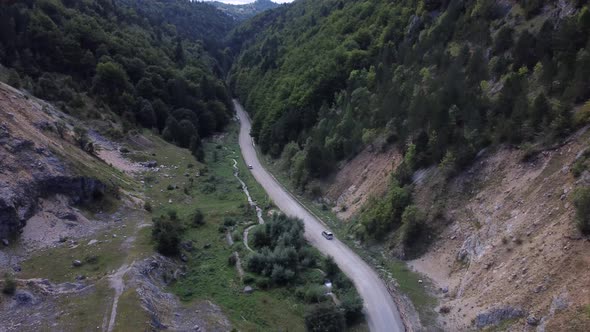 A Wide Drone Shot Tracking a Car Driving a Road Moving Through the Wilderness alt