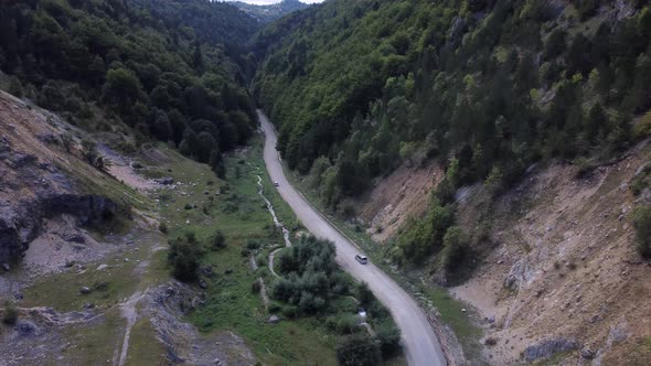 A Wide Drone Shot Tracking a Car Driving a Road Moving Through the Wilderness