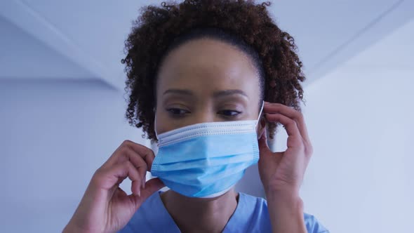 Portrait of mixed race female doctor putting face mask on alt