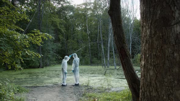 People Wearing Protective White Suits Taking Soil and Water Samples for Testing alt