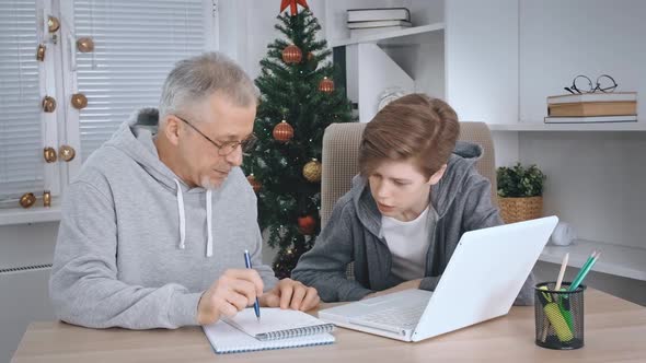 A Middleaged Father Helps His Teenage Son a Schoolboy to Study Online at Home Sitting at His Desk at