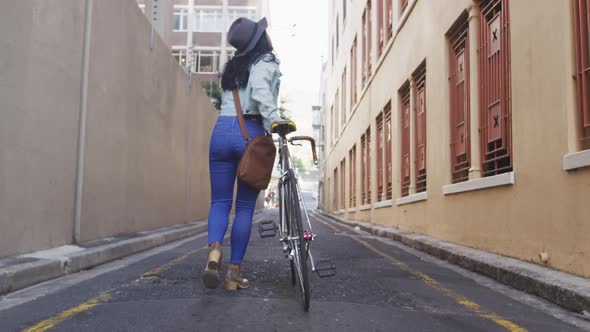 Mixed race woman walking next to her bike on the street alt