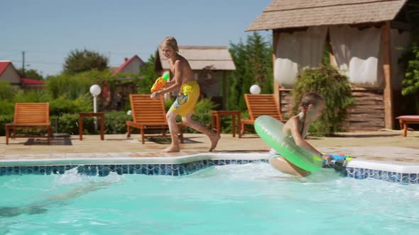 Four Caucasian Kids Playing Near Pool with Water Pistols and Inflatable Tubes in Slowmotion alt