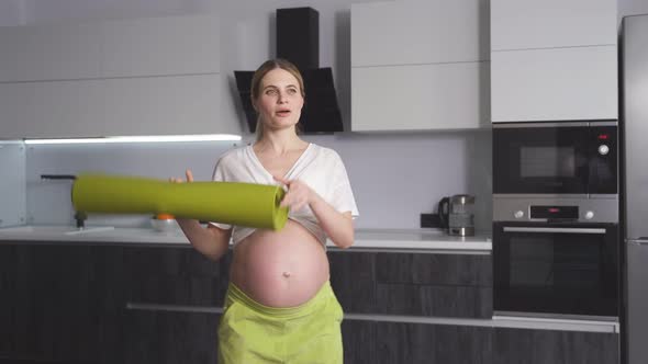 Closeup of a Pretty Pregnant Woman Standing with a Fitness Mat in Her Living Room