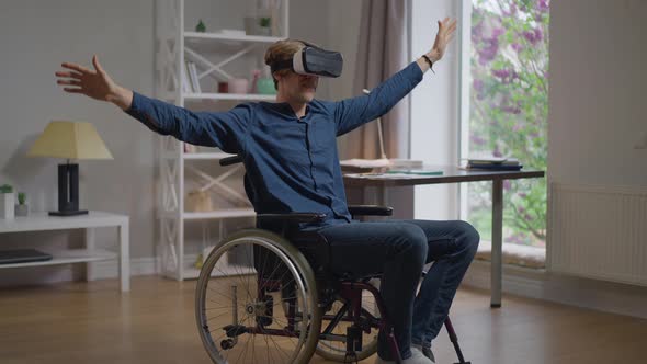 Smiling Happy Disabled Man in VR Headset Enjoying Augmented Reality Sitting in Wheelchair at Home alt