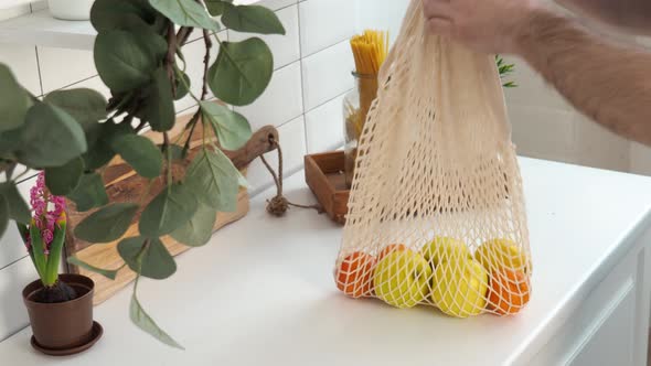 The hands of a young man put an eco friendly string bag with juicy ripe tangerines
