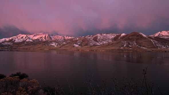 Time lapse of low clouds lighting up as sun rises and shines on mountain alt