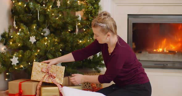 Woman Positioning Christmas Presents Under The Tree alt