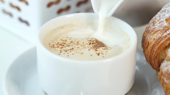 Milk is Poured From Milk Jug Into Cup of Cappuccino Coffee with Creamy Foam on Background of Fresh alt