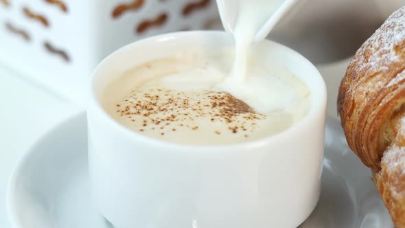 Milk is Poured From Milk Jug Into Cup of Cappuccino Coffee with Creamy Foam on Background of Fresh