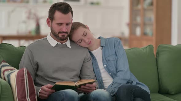 Man Reading Book While Wife is Sleeping on Sofa alt