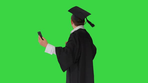Smiling Male Student in Graduation Gown Showing Campus Via Video Call on His Phone on a Green Screen alt