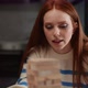 Closeup of Focused Young Redhaired Woman Carefully Taking Jenga Wooden Block From Bottom of Tower - VideoHive Item for Sale