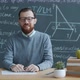 Portrait of University Professor Sitting at Desk in Class with Chalkboard in Background - VideoHive Item for Sale