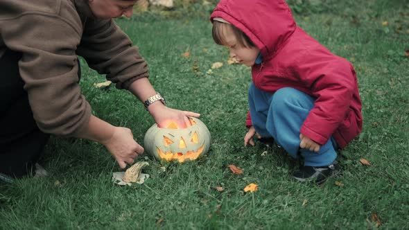 Mom and a Cute Little Girl are Lighting Candles Inside a Pumpkin for Halloween alt