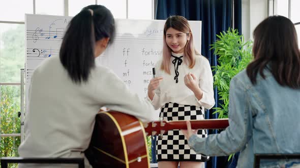 young Asian music teacher is teaching note reading and guitar chords correctly
