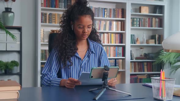 Young Pretty Indian Woman Reads Paper Report Via Phone Video Call alt
