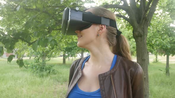 Beautiful Cheerful Woman Uses A Modern Helmet Of Virtual Reality In The Park alt