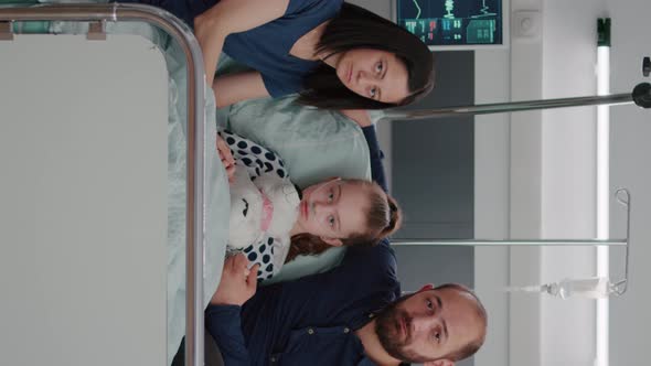 Vertical Video Portrait of Worried Family Looking Into Camera in Hospital Ward During Therapy alt