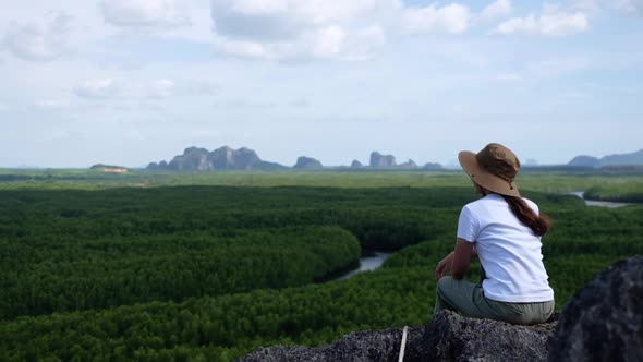 A woman sitting on the mountain peak while traveling the mangrove forest viewpoint