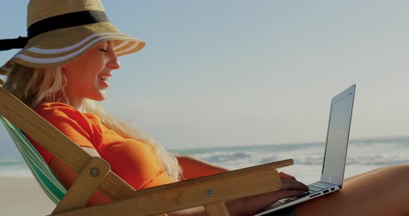 Woman with hat using laptop at beach in the sunshine 