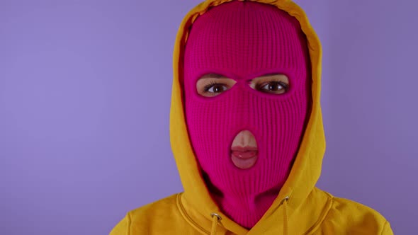 Close Up of Unrecognizable Woman in Pink Balaclava Shows Her Tongue on Purple Background alt