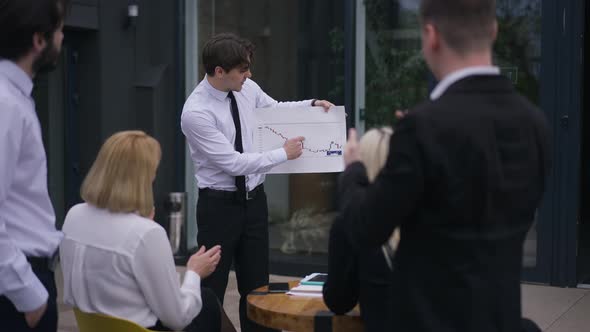 Portrait of Positive Smiling Man Showing Graph to Colleagues Clapping Supporting Coworker alt