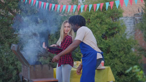 Side View of African American Man Making Bbq and Discussing Startup Idea with Caucasian Woman alt