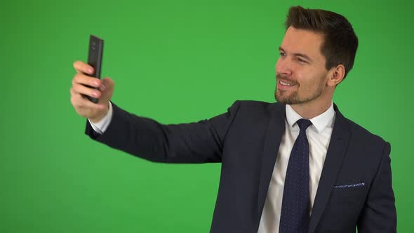 A Young Handsome Businessman Takes Selfies with a Smartphone - Green Screen Studio alt