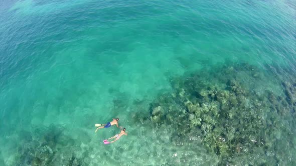 Aerial view of a man and woman couple snorkeling over a coral reef of a tropical island. alt