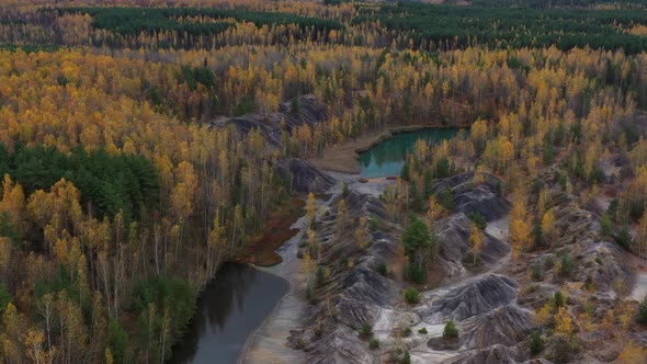 Flying above the abandoned quarry with forest and lake in autumn.