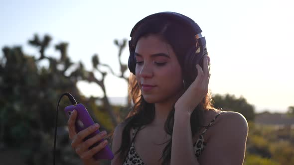 A beautiful young hispanic woman holding a smartphone listening to music on headphones outdoors in e alt