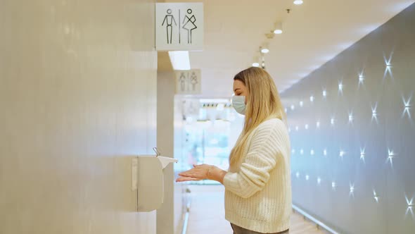 a Young Woman in a Protective Mask Presses a Diffuser with an Antiseptic alt