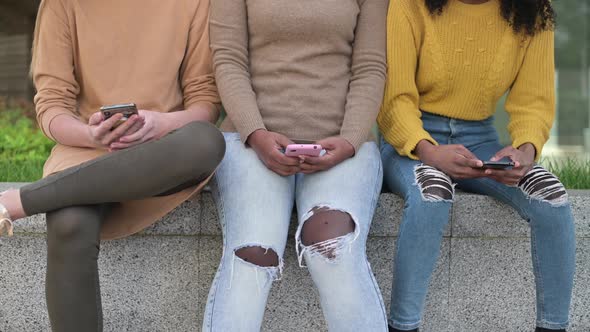 Three young women with phones in their hands are sitting on the parapet alt