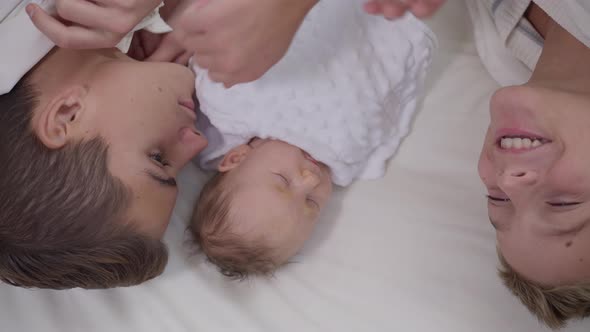 Top View Adorable Baby Girl Lying on White Bed with Teenage Boys Talking Smiling in Slow Motion alt