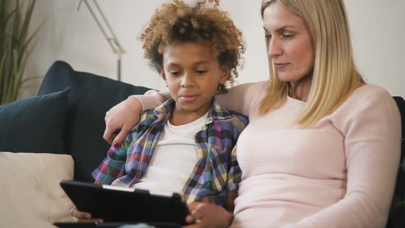 Mother and Son Is Sitting on Couch and Watching Funny Education Video on Laptop alt
