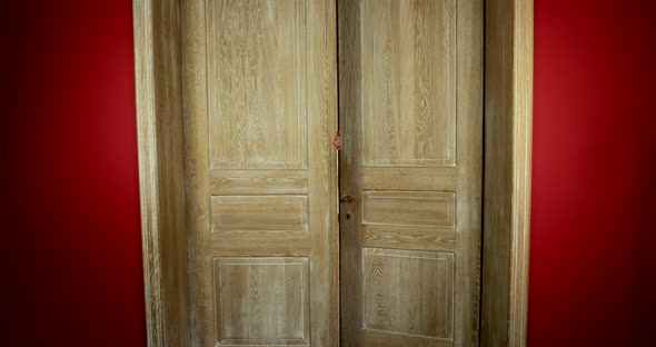 Hospitable woman opening double wooden door welcoming guests. Static, interior. alt
