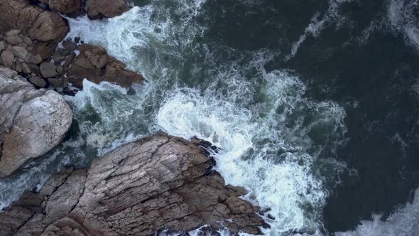 Aerial view over waves breaking onto rocks in the ocean
