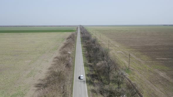 Aerial View of a Lone White Car Driving on a Rural Highway Surrounded By Fields alt