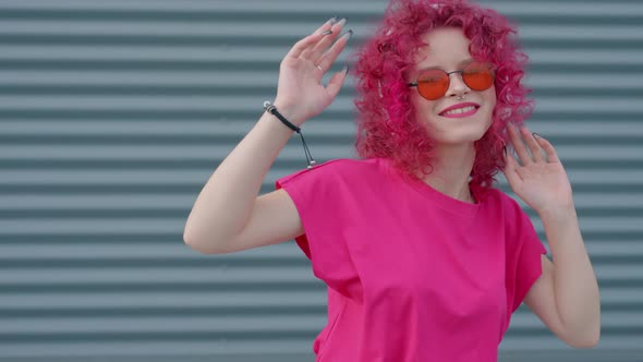 A Pink Curly Girl in Headphones is Listening to Music and Dancing alt