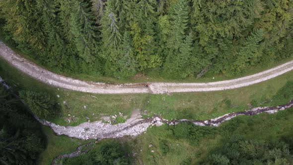 Top Down Aerial View of a Hiker Walking Across a Curved Trail Road in Summertime